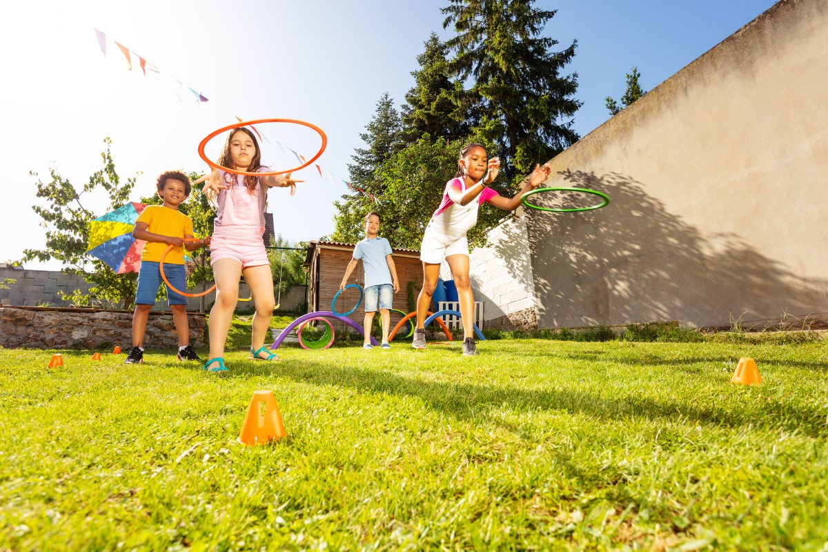 Group of divers kids aiming to throw circle sports hoops to the target cone playing game on the lawn